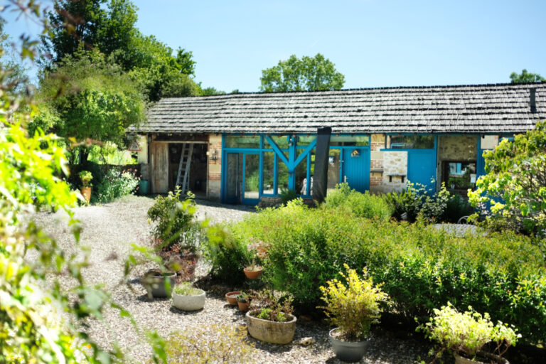 Bijgebouw met groene tuin ervoor en blauwe kozijnen en deuren.