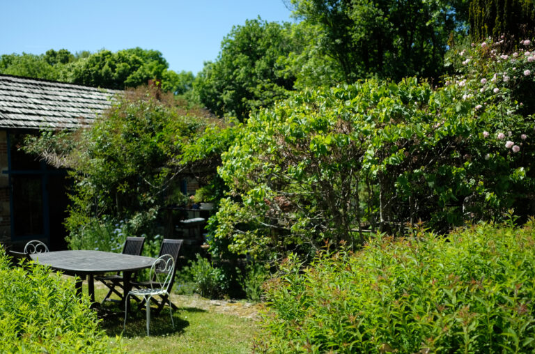 De grote tuin van L'école Buissonnière met veel groen en een mooie tuintafel met stoelen.